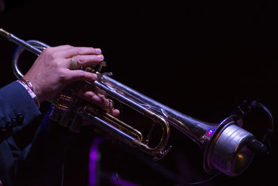 Cropped hands of man playing trumpet at night