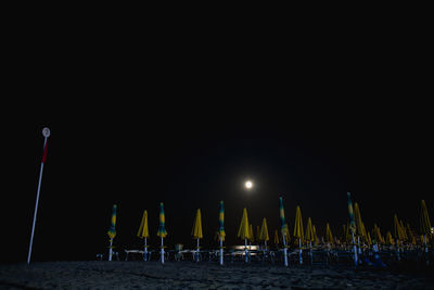 Row of illuminated chairs on beach against clear sky at night