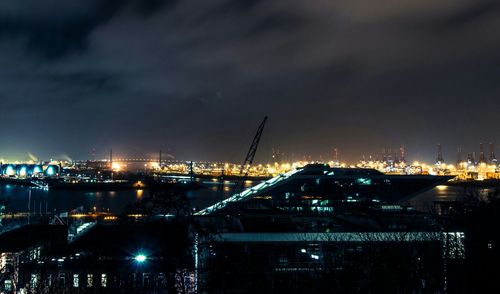 Illuminated cityscape by sea against sky at night