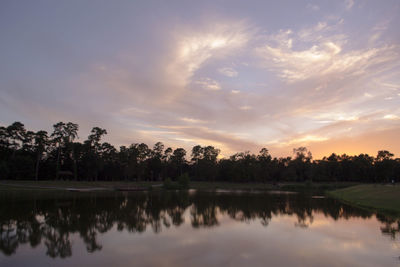 Reflection of trees in calm lake at sunset