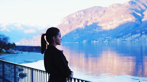 Side view of woman standing by railing against lake