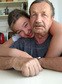 Smiling granddaughter embracing grandfather at home