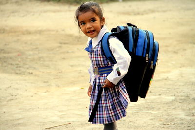 Cute schoolgirl with backpack standing on field