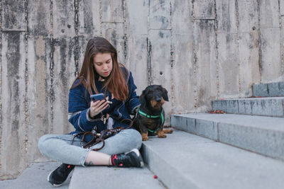 Young adult woman looking her smartphone stairs sit next to her dog