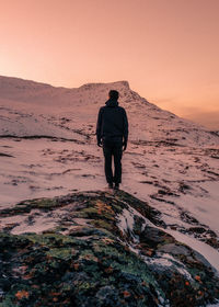 Rear view of man standing on shore during sunset