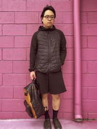 Portrait of young asian man in eyeglasses standing in front of pink brick wall.