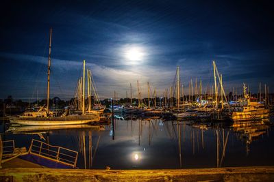 Sailboats moored on harbor against sky at night