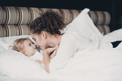 Mother and daughter touching noses while lying on bed