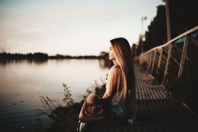 Profile view of thoughtful young woman sitting on boardwalk at lake
