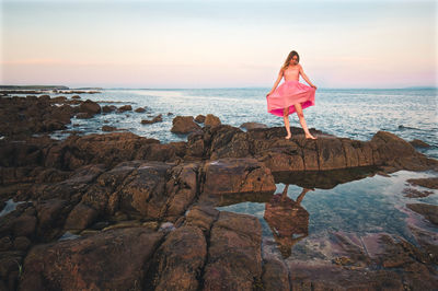 Beautiful young girl in pink dress standing on the rocky coast of wild atlantic way at barna