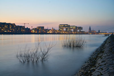 Scenic view of the rhine by illuminated cologne against sky at sunset