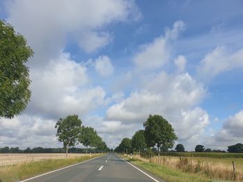 Empty road amidst field against sky