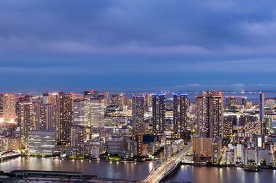 Illuminated city by river against sky at night