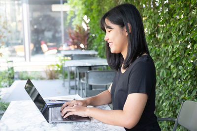 Side view of woman using phone while sitting on table