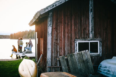 Male and female friends talking outside cottage in front of lake against sky during sunset