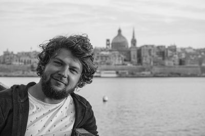 Portrait of smiling young man against river in city