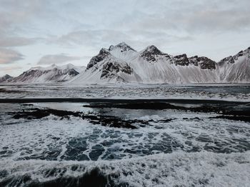 Scenic view of sea by snowcapped mountains against sky