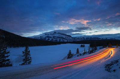 Light trails on road by mountain against sky at night