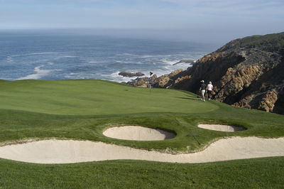 Scenic view of golf course by sea against sky