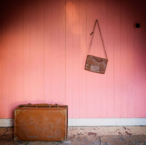 Damaged suitcase against leather bag hanging on pink wall