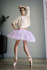 Charming ballerina poses showing her legs in the room in front of the mirror in pointes and tutu