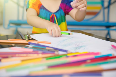 Midsection of woman holding multi colored pencils on table