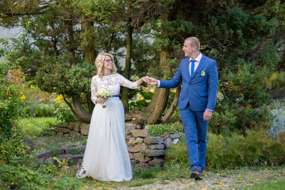 Happy wedding couple holding hands while walking against plants at park