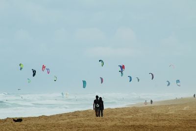 People at beach against sky and parachutes