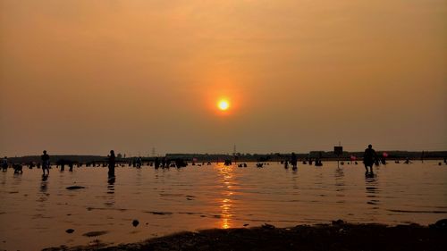 Silhouette people on beach against sky during sunset