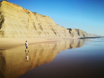 Boy walking towards sea at beach against mountains