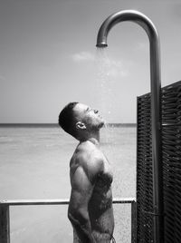 Profile view of shirtless muscular man taking shower at beach