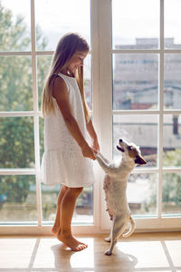 Girl in a white dress stands on the windowsill with a dog
