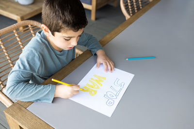 Little kid drawing stop war on a paper. ukraine russia war concept.