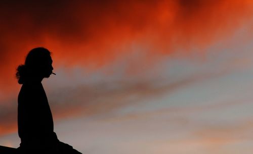 Silhouette of woman against orange sunset sky