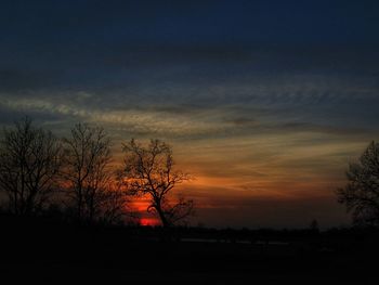 Silhouette trees on landscape against sky at sunset