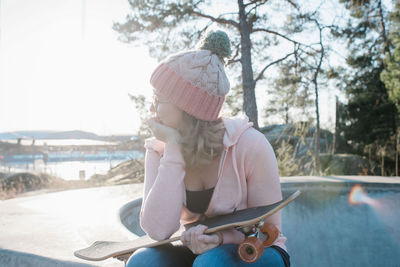 Woman sat thinking holding her skateboard in a skatepark at sunset