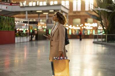 Woman holding smart phone and shopping bags at station