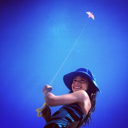 Low angle view of smiling girl flying kite against clear blue sky