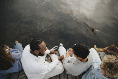 High angle view of male and female friends having fun while sitting on pier near lake