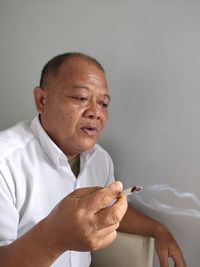 Portrait of indonesian man smoking cigarette against white background.