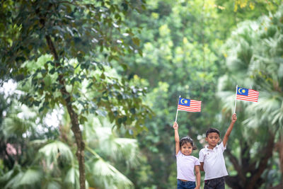 Woman standing by flag against trees