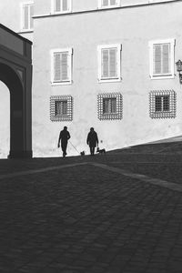 Rear view of people walking on street by building