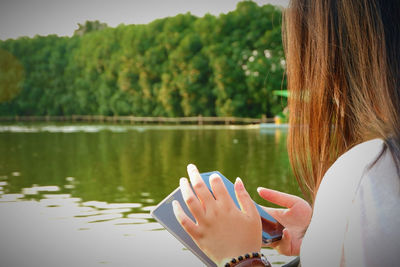 Midsection of woman using smart phone by lake