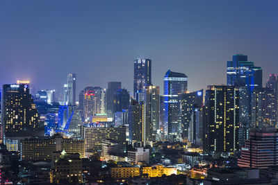 Illuminated modern buildings in city against sky at night