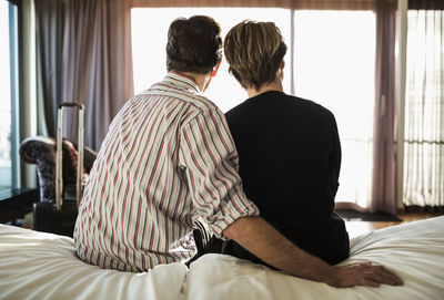 Rear view of business couple sitting on bed in hotel room