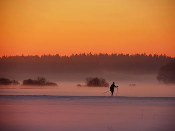 Silhouette man skiing on field against clear orange sky during sunset