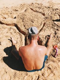 Rear view of shirtless man sitting on sand