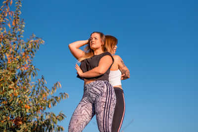 Low angle view of women in sports clothing against clear sky