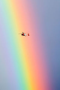 Low angle view of helicopter flying against rainbow