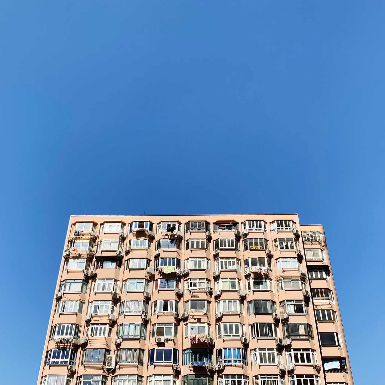 low angle view, clear sky, architecture, copy space, built structure, building exterior, blue, sky, building, day, window, no people, nature, in a row, sunlight, side by side, pattern, outdoors, order, abundance, apartment